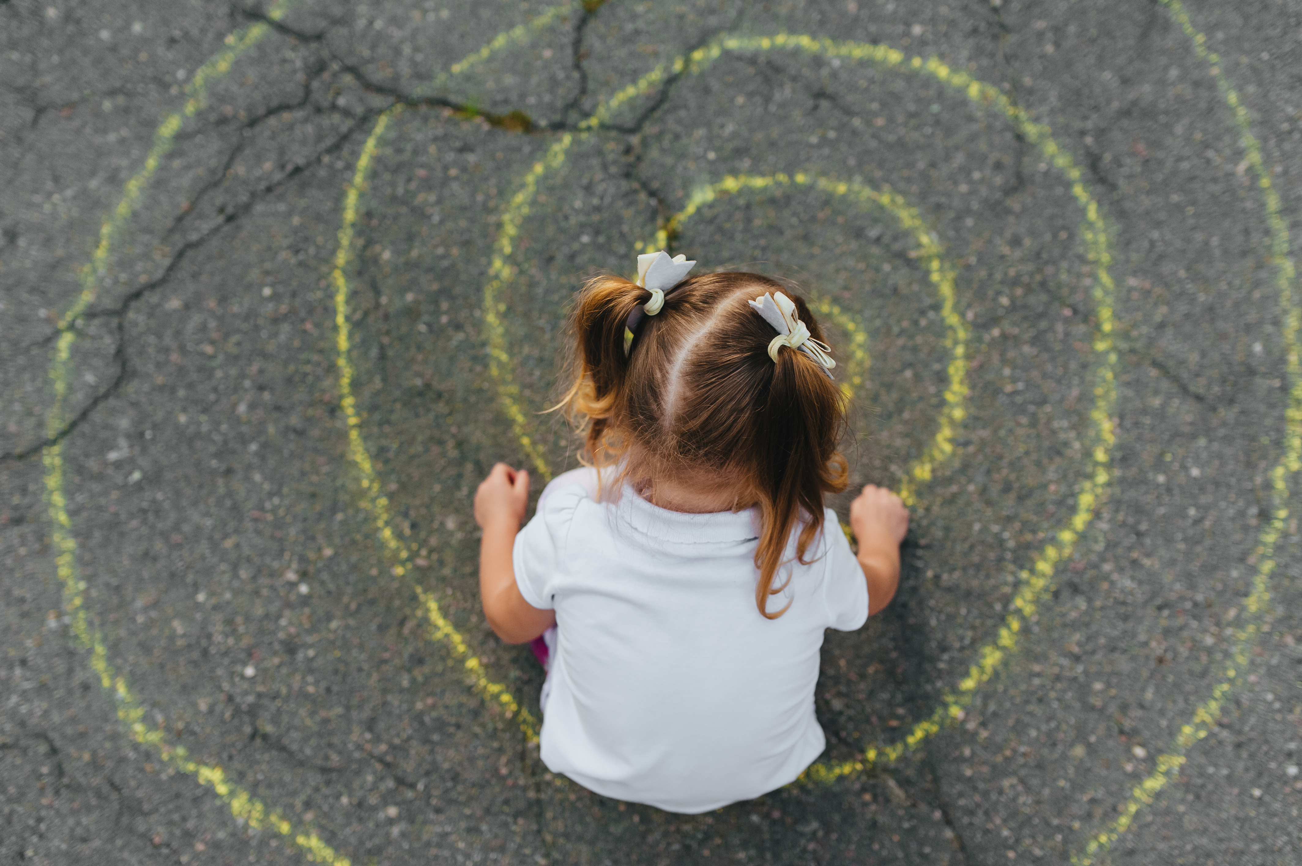 preschooler draws chalk spiral on asphalt
